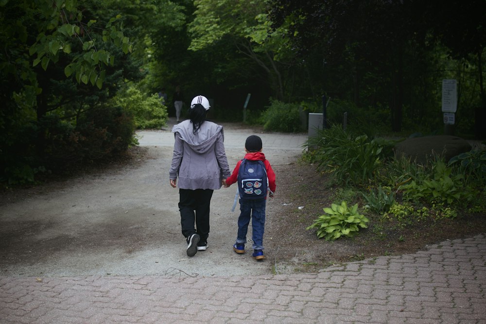 A parent and child walking hand in hand along a park path