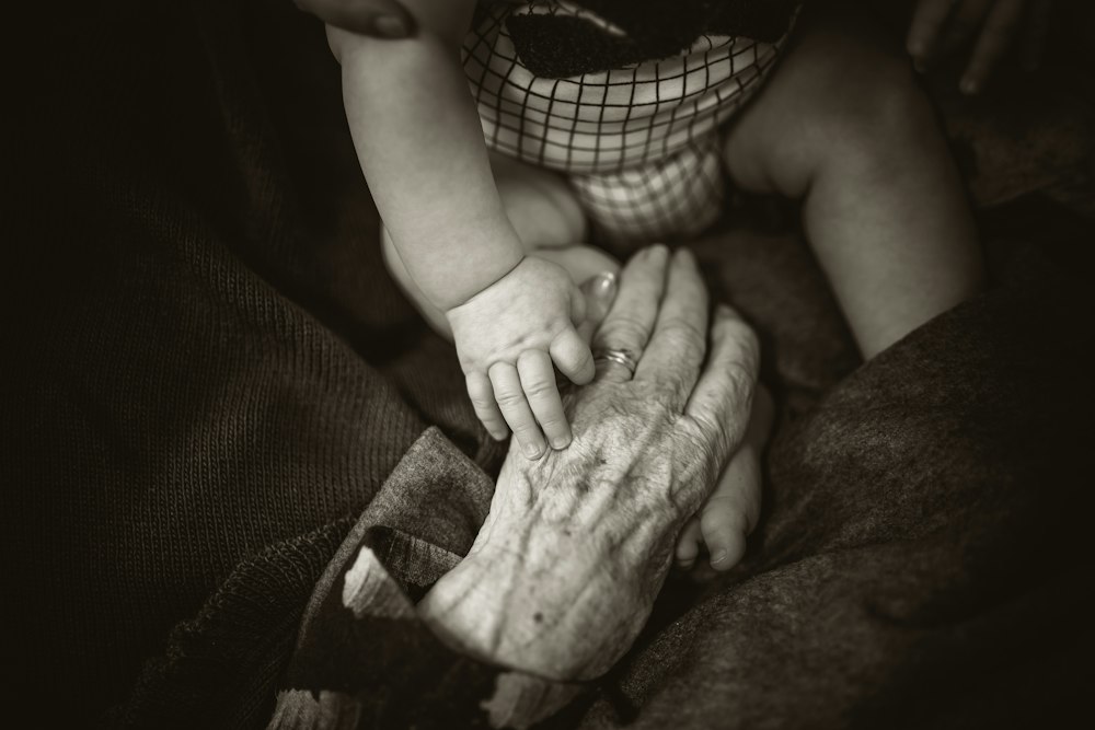 An older hand gently holding a baby's hand